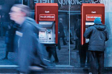 An individual walks quickly by a red ATM