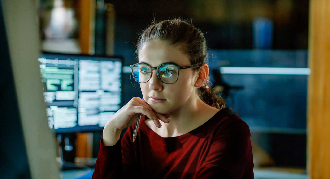 A woman gazes at code scrolling through a computer monitor