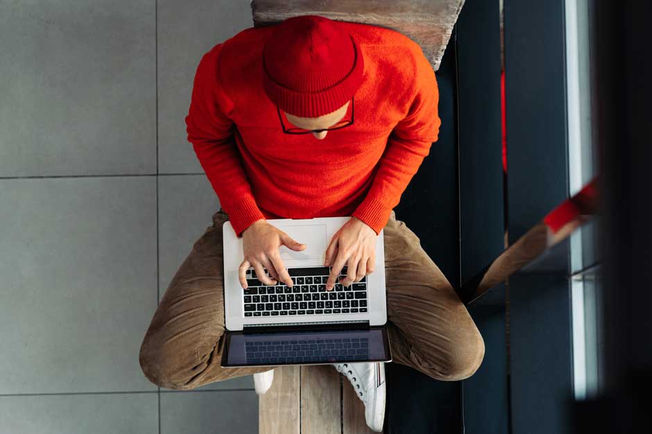 A seated man types on a laptop in his lap.