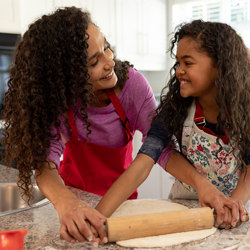 A mother and daughter, both with brown curly hair, bake cookies together