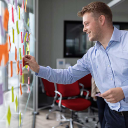 A man smiles as he posts colored sticky notes onto a window